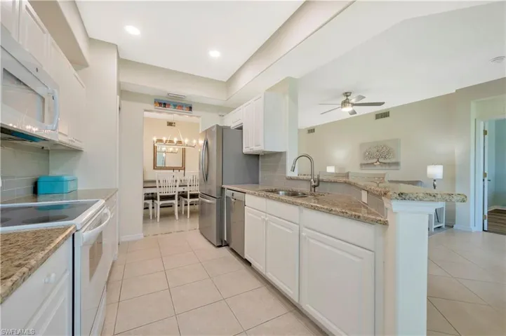 Kitchen featuring stainless steel appliances, light stone counters, white cabinetry, and light tile patterned flooring