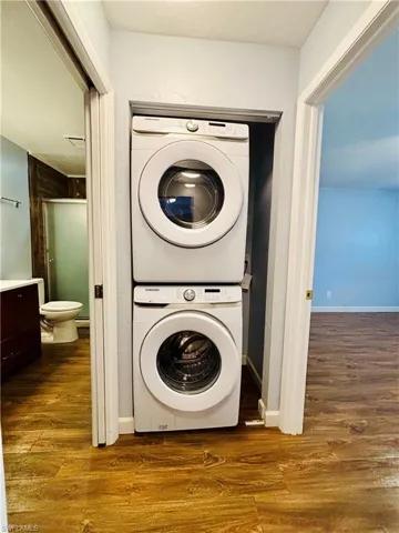 Laundry room featuring stacked washing machine and dryer and dark wood finished floors