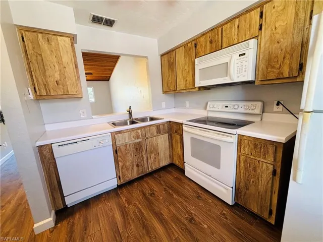Kitchen with white appliances, light countertops, dark wood-style flooring, and brown cabinets