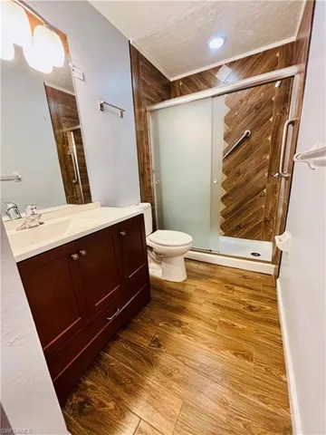 Full bath with vanity, dark wood-style floors, a shower stall, and a textured ceiling