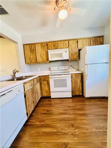 Kitchen featuring white appliances, light countertops, dark wood-type flooring, and brown cabinets