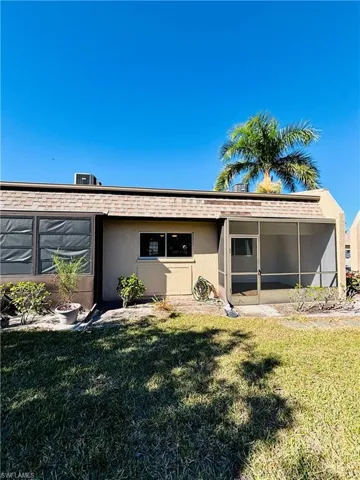 Rear view of house with stucco siding, a lawn, and a sunroom