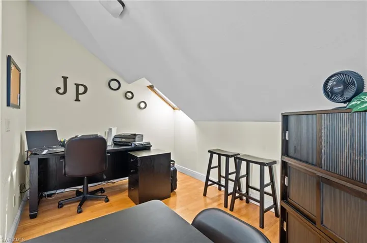 Home office with baseboards, vaulted ceiling, and light wood-type flooring