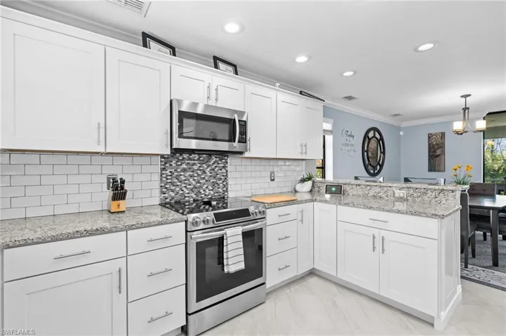 Kitchen featuring tasteful backsplash, ornamental molding, stainless steel appliances, white cabinets, and a peninsula