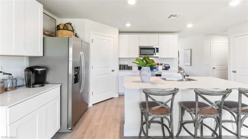 Model home. Kitchen with white cabinetry, a breakfast bar area, stainless steel appliances, light wood-type flooring, and a kitchen island with sink