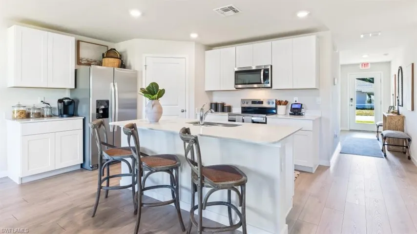 Model home. Kitchen with stainless steel appliances, white cabinetry, light wood finished floors, an island with sink, and recessed lighting