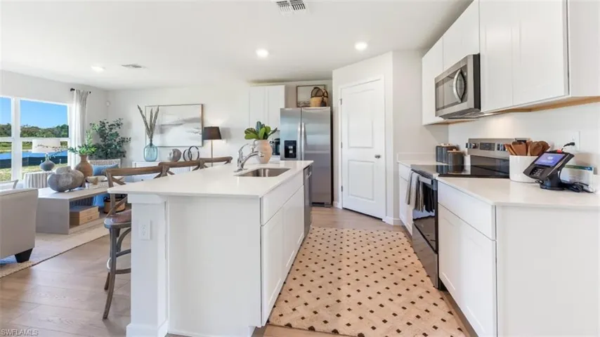 Model home. Kitchen featuring white cabinetry, stainless steel appliances, a kitchen breakfast bar, a center island with sink, and recessed lighting
