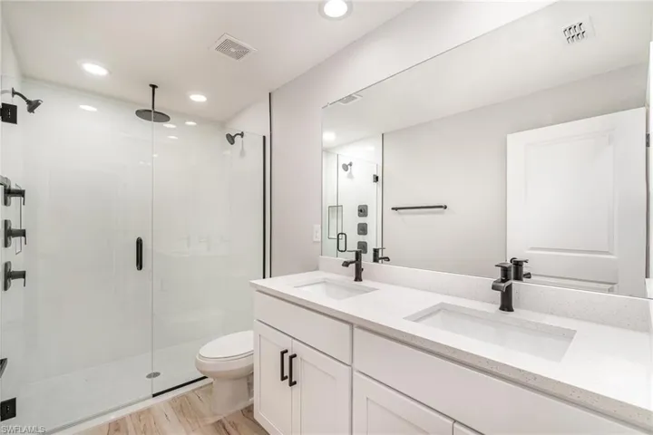 Bathroom featuring toilet, a shower with door, wood-type flooring, and double vanity