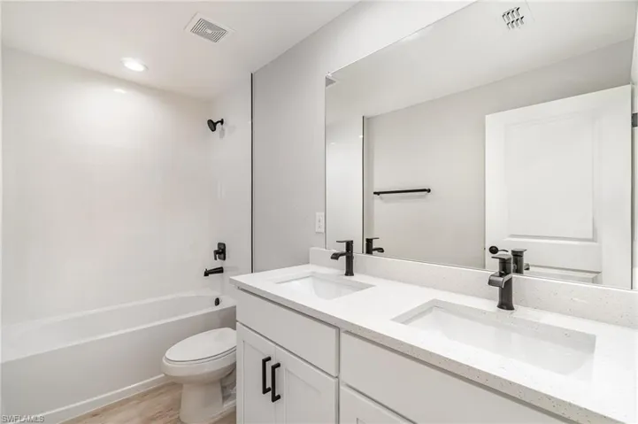 Full bathroom featuring double vanity, shower / bath combination, toilet, and hardwood / wood-style floors