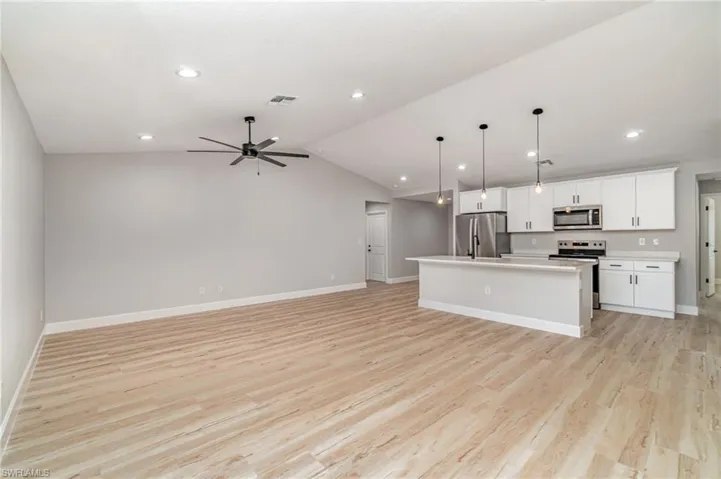Kitchen with appliances with stainless steel finishes, light hardwood / wood-style flooring, lofted ceiling, and a center island with sink