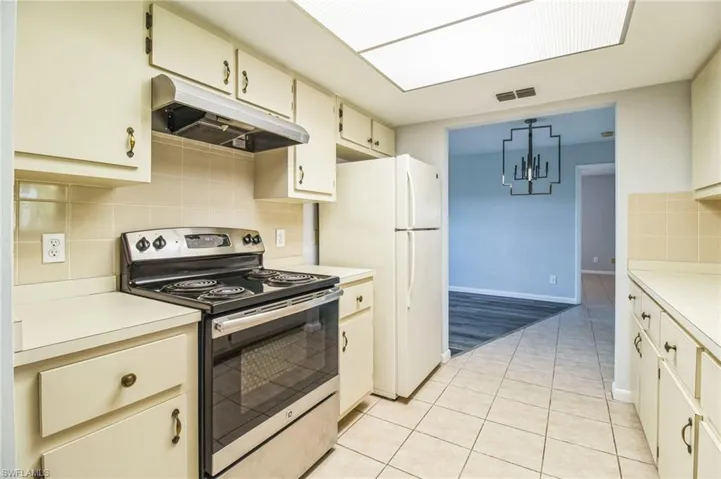 Kitchen with pendant lighting, light tile patterned flooring, electric stove, decorative backsplash, and white fridge