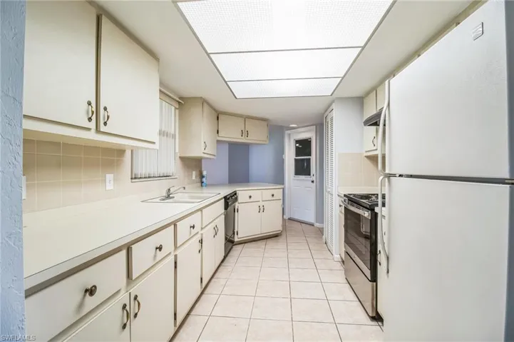Kitchen with decorative backsplash, appliances with stainless steel finishes, extractor fan, sink, and light tile patterned flooring