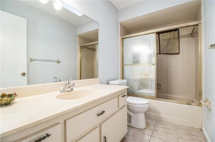 Full bathroom with tile patterned floors, shower / bath combination with glass door, vanity, and toilet