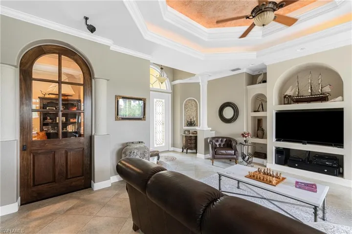 Living room featuring ornate columns, ceiling fan, crown molding, and built in features