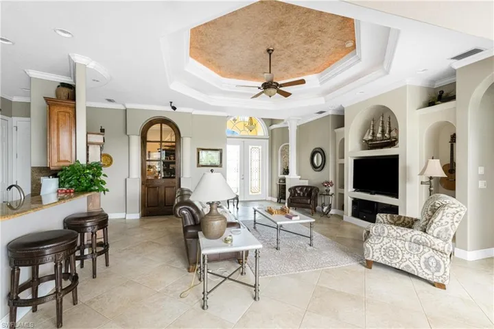 Living room featuring ceiling fan, built in shelves, light tile patterned flooring, a raised ceiling, and crown molding