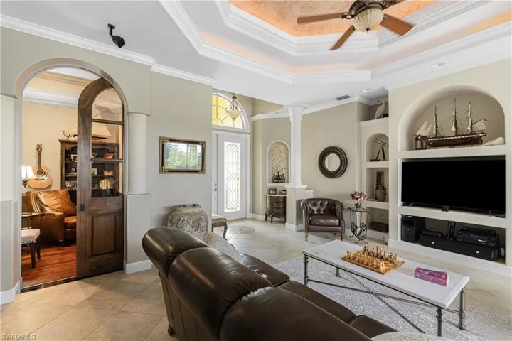 Tiled living room with built in shelves, ornamental molding, and ceiling fan