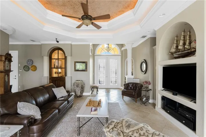 Tiled living room with built in shelves, ornamental molding, and ceiling fan