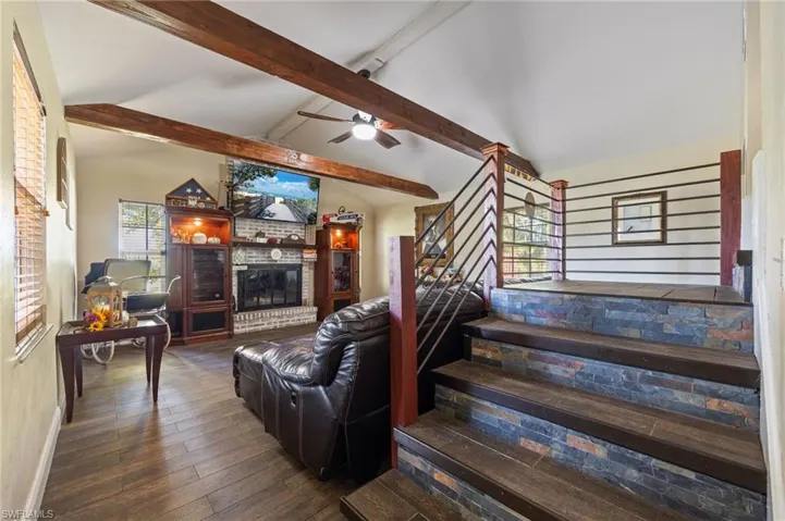 Living room with a brick fireplace, dark wood finished floors, stairway, and ceiling fan