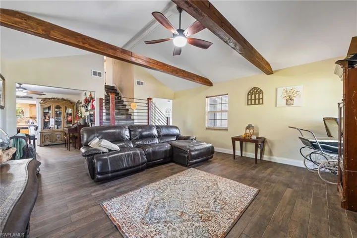 Living room featuring a ceiling fan, stairs, beamed ceiling, dark wood finished floors, and high vaulted ceiling