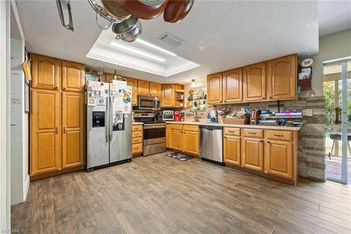 Kitchen featuring open shelves, brown cabinets, appliances with stainless steel finishes, dark wood-style flooring, and light countertops