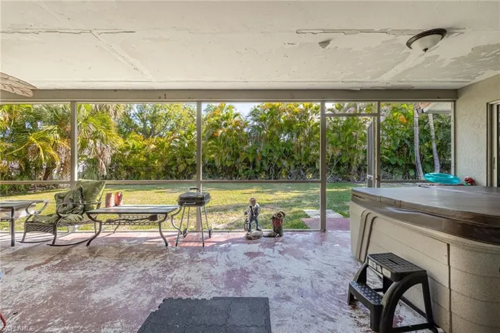 View of patio / terrace with a hot tub, a sunroom, glass enclosure, and view of scattered trees