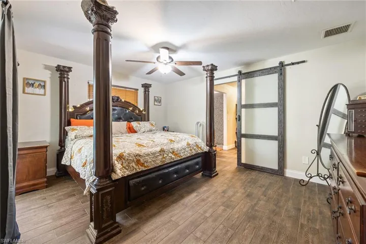 Bedroom with a barn door, dark wood-type flooring, and ceiling fan