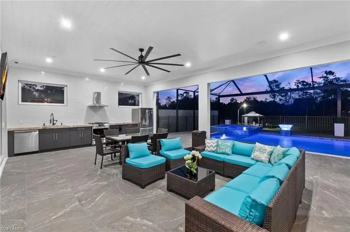View of patio featuring glass enclosure, exterior kitchen, an in ground hot tub, a sink, and an outdoor hangout area