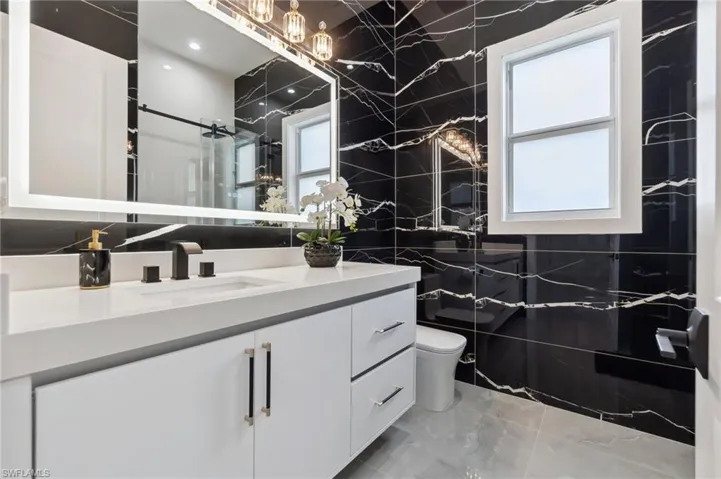 Bathroom with vanity, tile walls, toilet, and a wealth of natural light