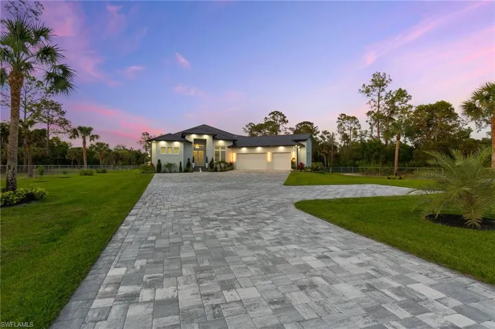 View of front facade featuring decorative driveway, a yard, fence, and an attached garage