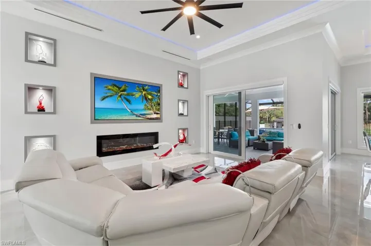 Living area featuring a glass covered fireplace, ornamental molding, baseboards, and ceiling fan