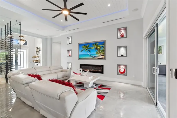 Living area featuring ceiling fan, baseboards, a tray ceiling, recessed lighting, and a glass covered fireplace