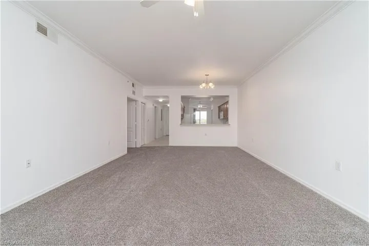 Unfurnished living room with ceiling fan with notable chandelier, carpet floors, baseboards, ornamental molding, and visible vents