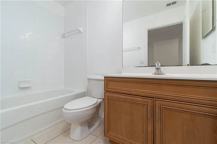 Full bathroom with tile patterned floors, bathing tub / shower combination, toilet, visible vents, and vanity