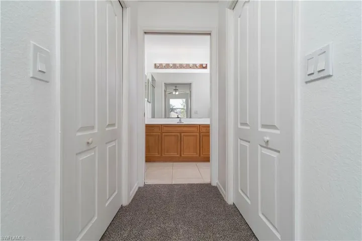 Hallway featuring light carpet, a textured wall, a sink, and light tile patterned floors