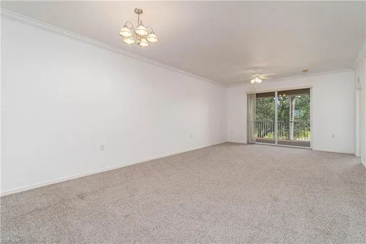 Carpeted spare room featuring baseboards, crown molding, and ceiling fan with notable chandelier