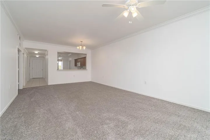 Carpeted empty room with crown molding, baseboards, and ceiling fan with notable chandelier