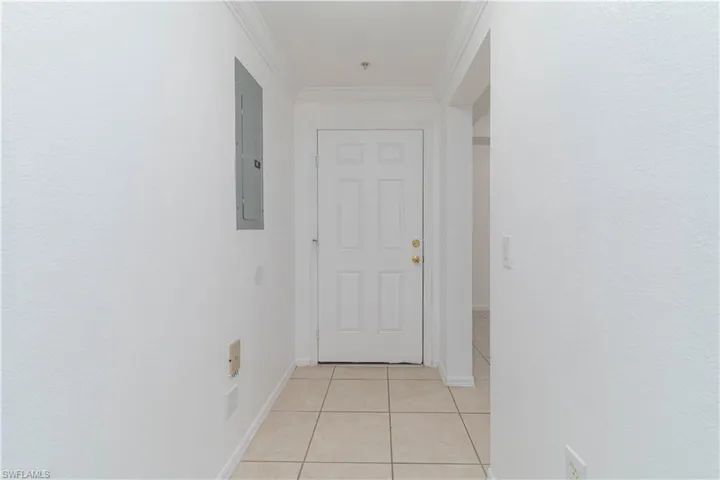 Corridor featuring electric panel, baseboards, light tile patterned floors, and crown molding