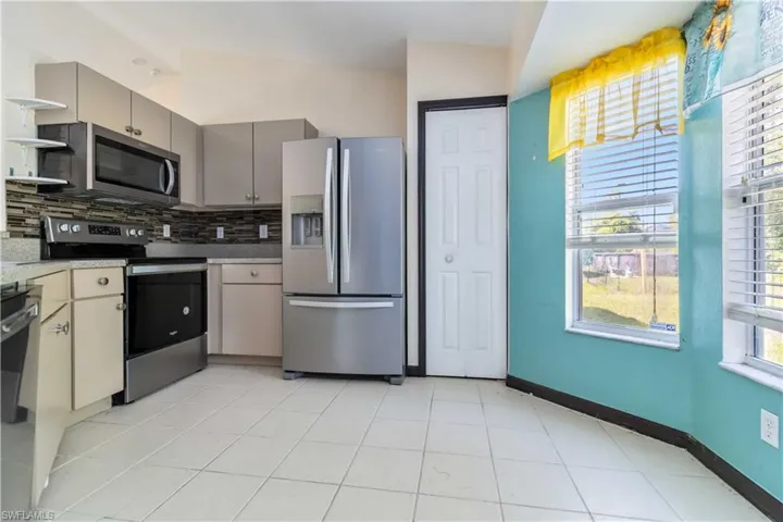 Kitchen with appliances with stainless steel finishes, light tile patterned floors, decorative backsplash, gray cabinets, and light countertops