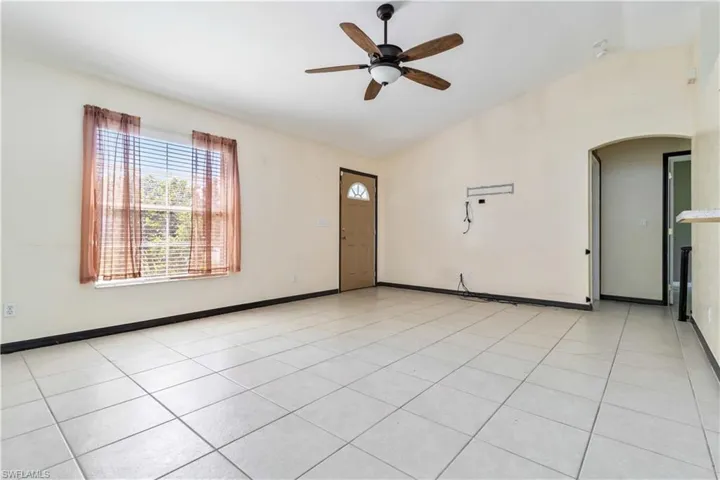 Unfurnished room featuring lofted ceiling, light tile patterned flooring, a ceiling fan, and arched walkways