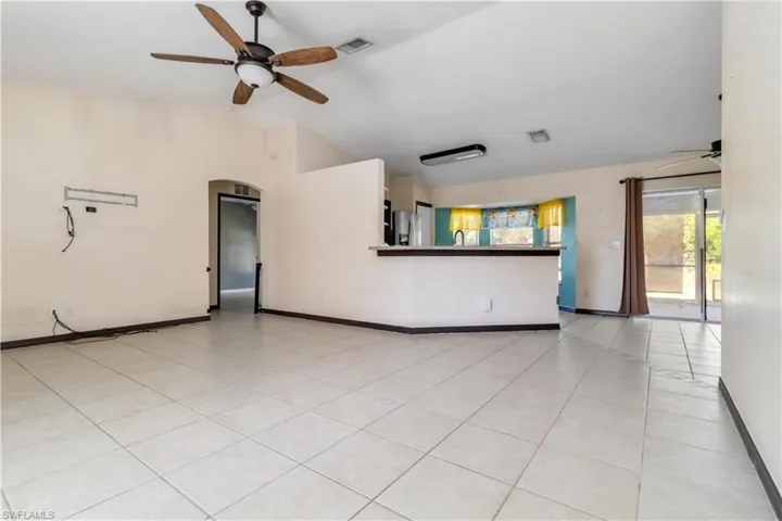 Unfurnished living room featuring a ceiling fan, light tile patterned flooring, vaulted ceiling, and arched walkways