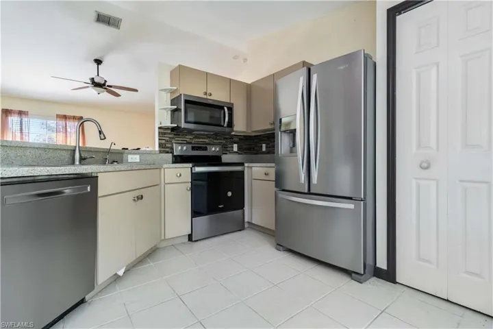Kitchen with appliances with stainless steel finishes, light tile patterned floors, tasteful backsplash, a ceiling fan, and light stone counters