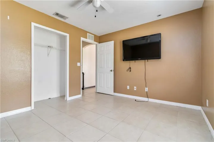 Unfurnished bedroom featuring arched walkways, light tile patterned floors, ceiling fan, and a closet