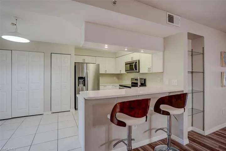 Kitchen with light countertops, a breakfast bar, appliances with stainless steel finishes, a peninsula, and white cabinetry