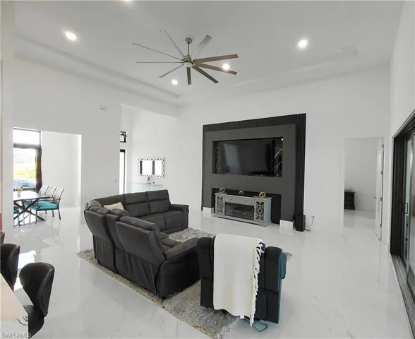 Spacious living area featuring polished tile flooring, a sleek entertainment wall with a mounted television and electric fireplace, and a contemporary ceiling fan