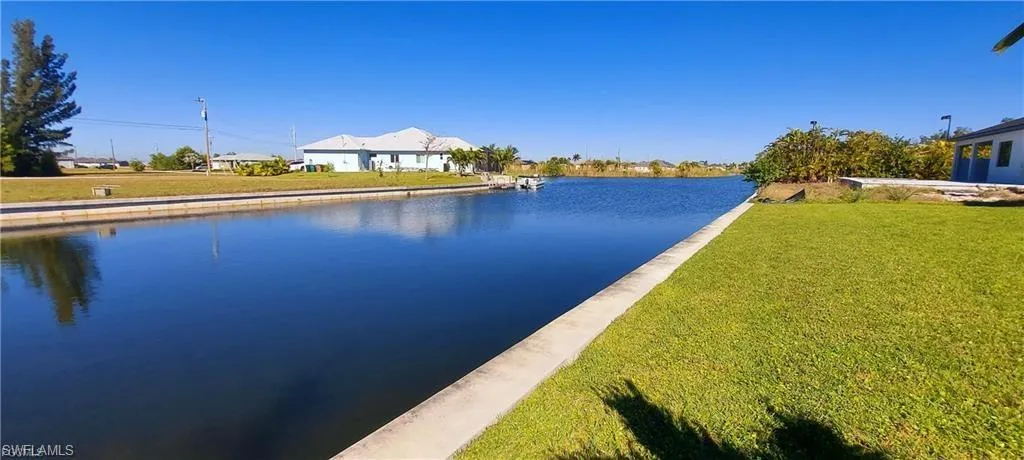 Waterfront property with a concrete seawall, expansive water views, and a well-maintained lawn