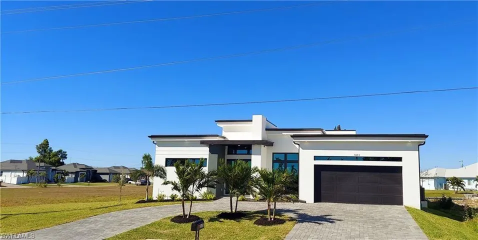 This property features a modern architectural style with a white exterior, a dark garage door, and a paved driveway