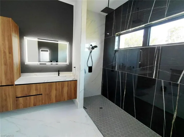 The bathroom features a modern vanity with light wood-tone cabinetry, a white countertop, and an illuminated mirror