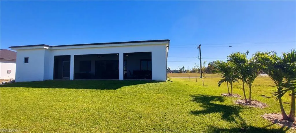 The property features a spacious rear yard with a manicured lawn, several young palm trees, and an expansive covered patio area
