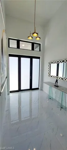 The entryway features high ceilings, a contemporary pendant light fixture, and large format polished tile flooring