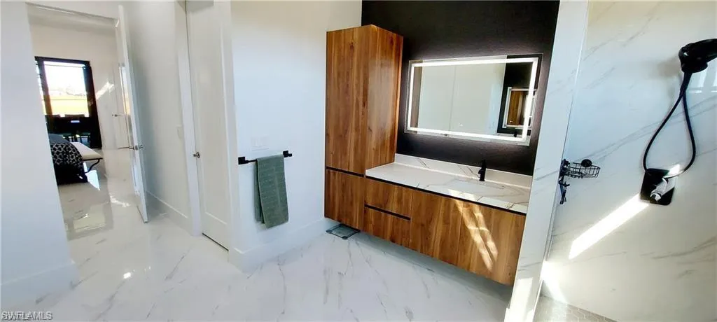 The bathroom features a modern vanity with a wood finish, a white countertop, and an illuminated mirror